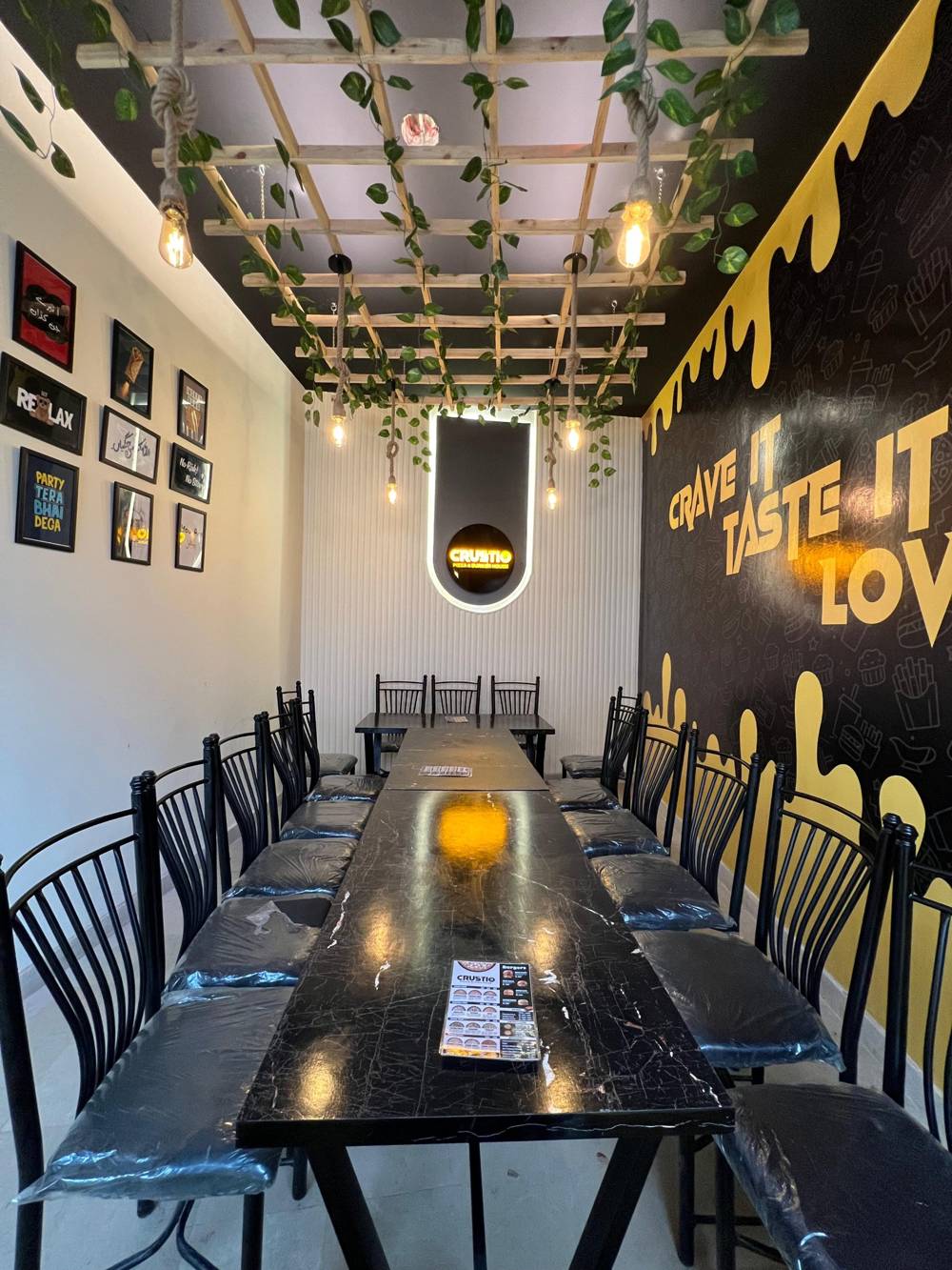 CRUSTIO dining room with a long black table, hanging vines and a gold drip wall